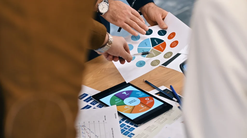 Business professionals collaborating at a table with a tablet and papers, focused on marketing outreach strategies