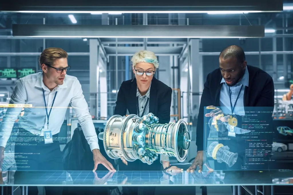 Colleagues analyze a computer screen displaying a mechanical part in a digital twin and virtual simulation context