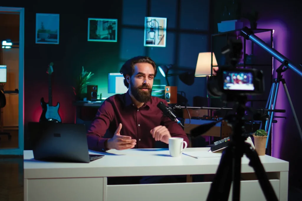 Man sitting at a desk with a laptop open and a camera positioned nearby, focused on content creation