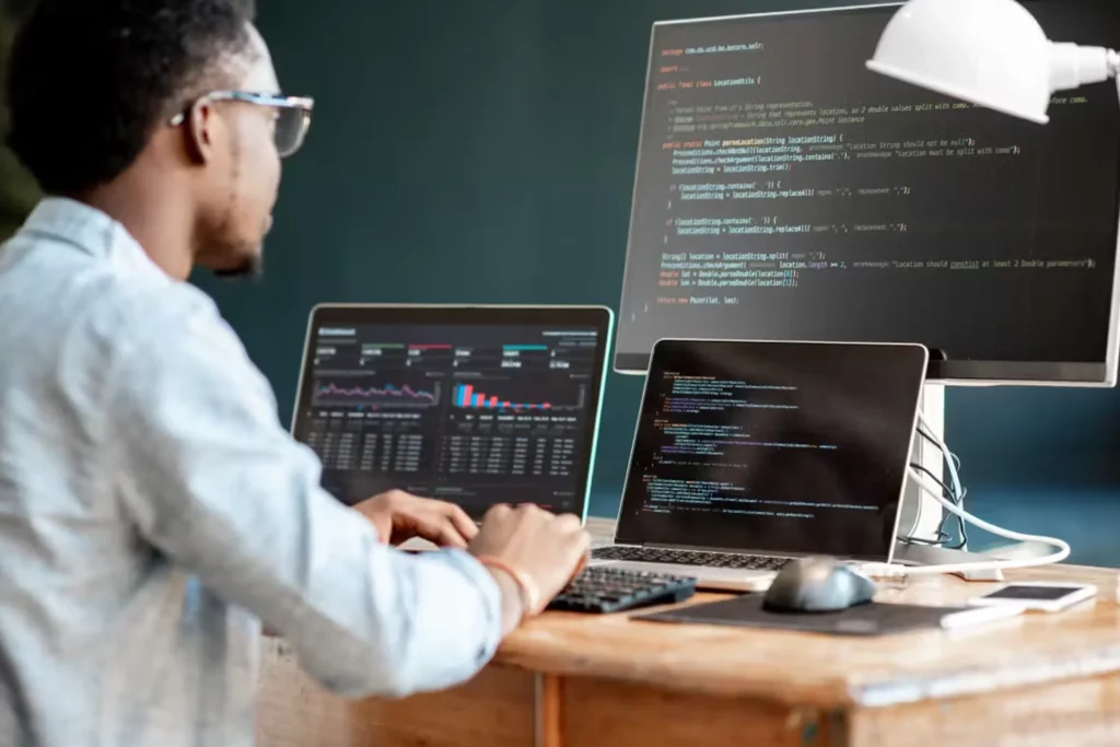 A man at a desk with two computers, engaged in tasks related to API and microservices architecture